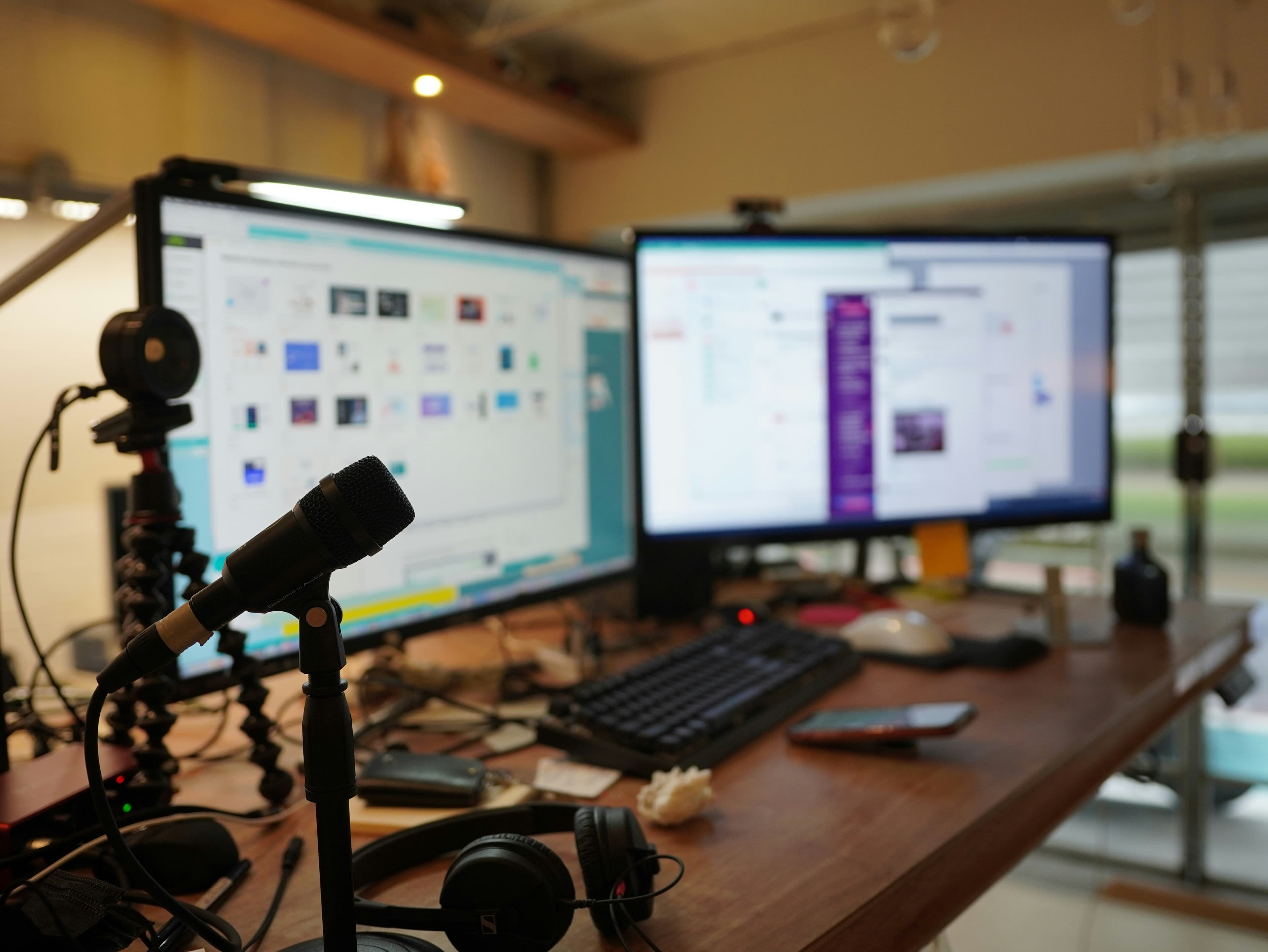 A streaming desk with dual monitors, keyboard and a broadcast microphone on a boom arm.