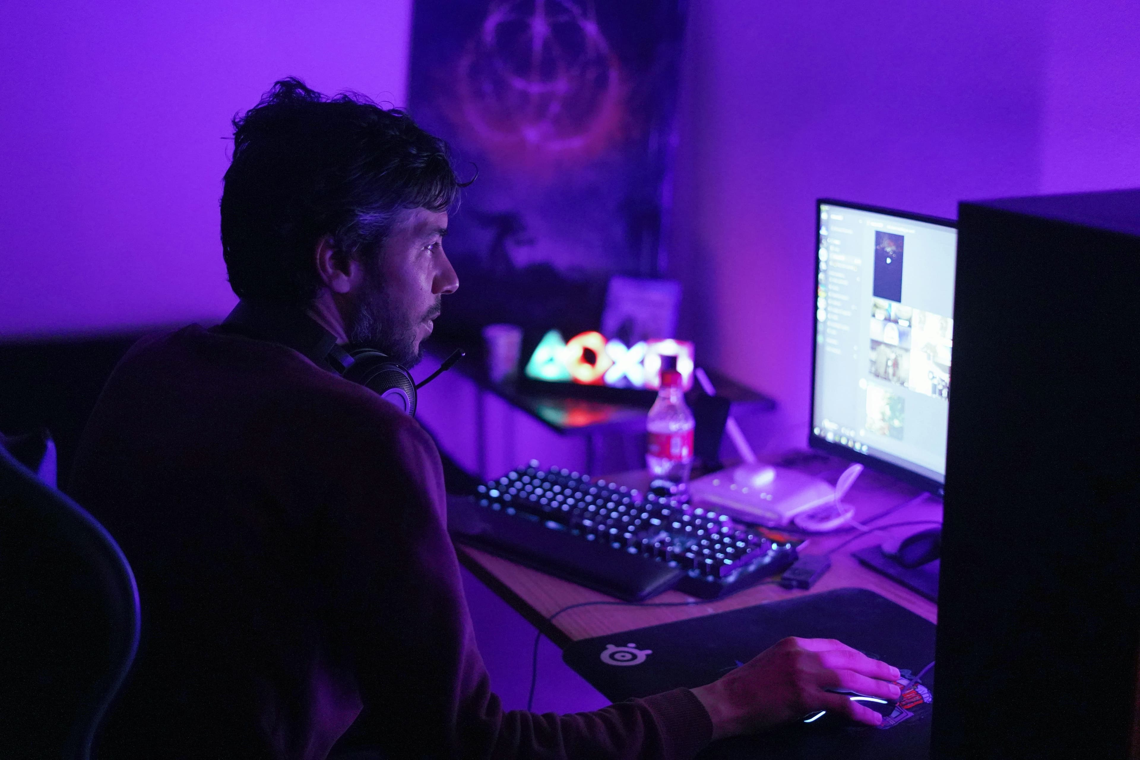 A creator at a streaming desk with colourful purple and blue lighting, multiple monitors and a microphone during a LIVE session.