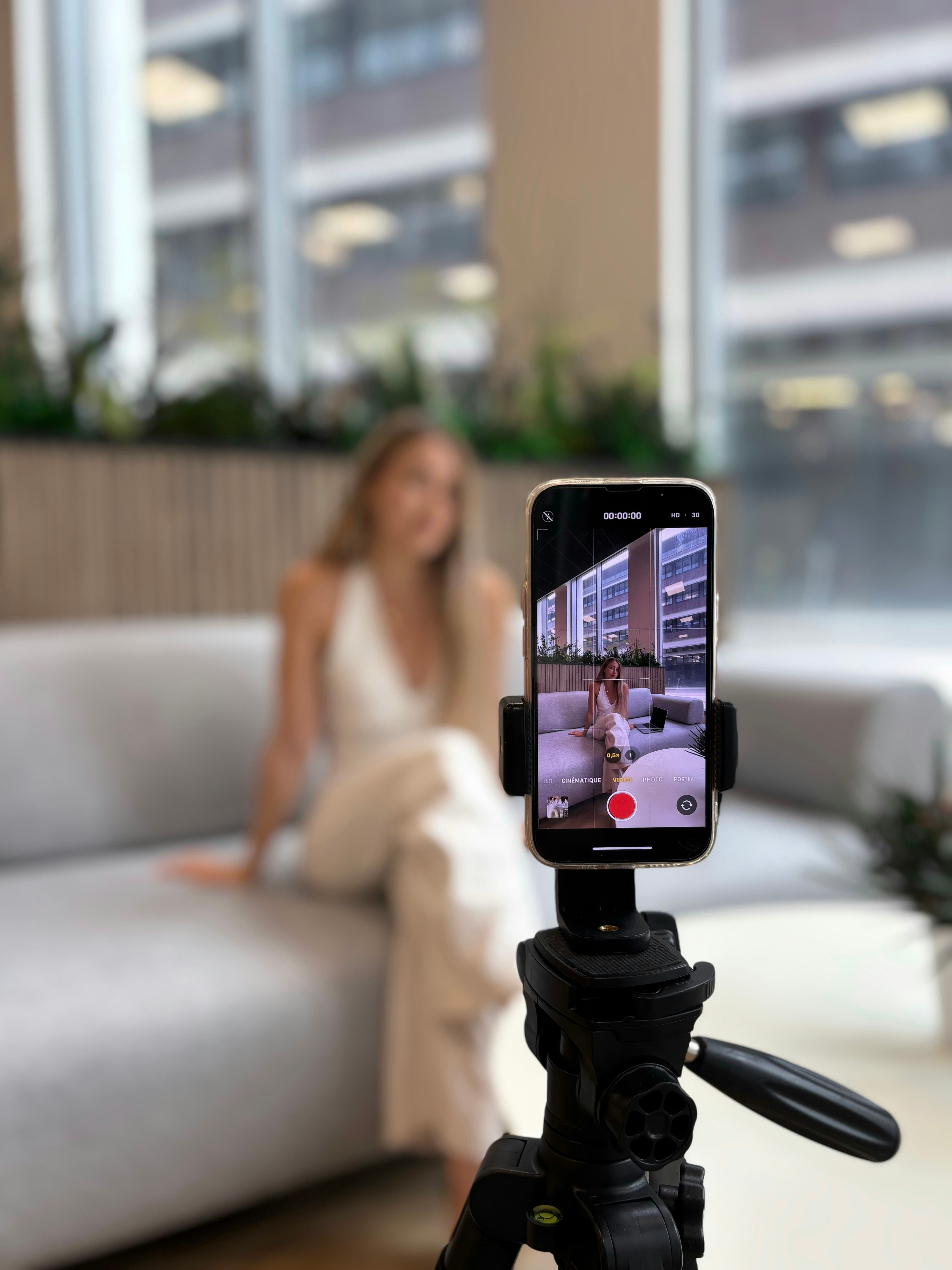 A creator recording herself on a smartphone mounted on a tripod in a bright space.