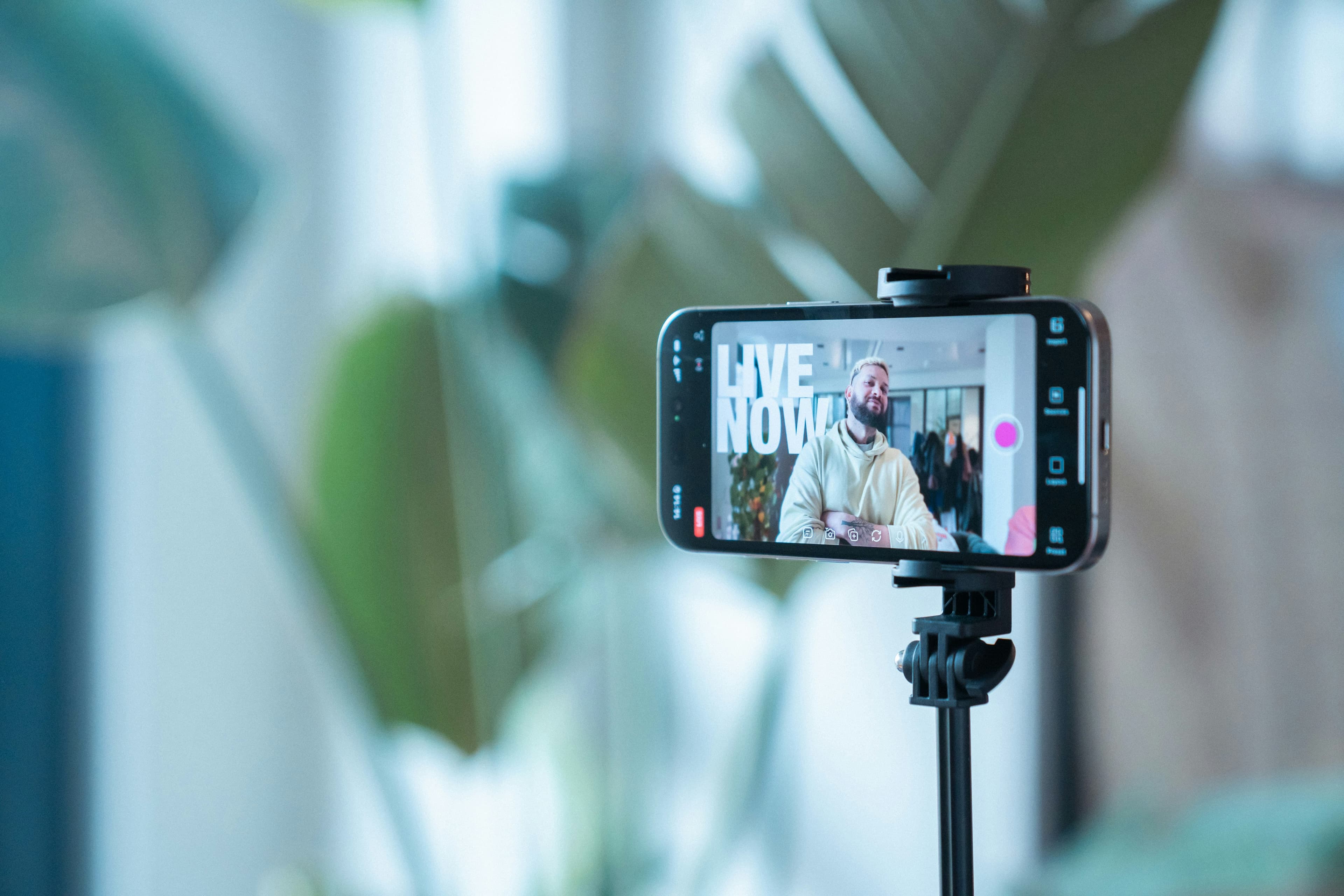 A smartphone recording a creator speaking during a live stream, with studio lighting and production gear visible.