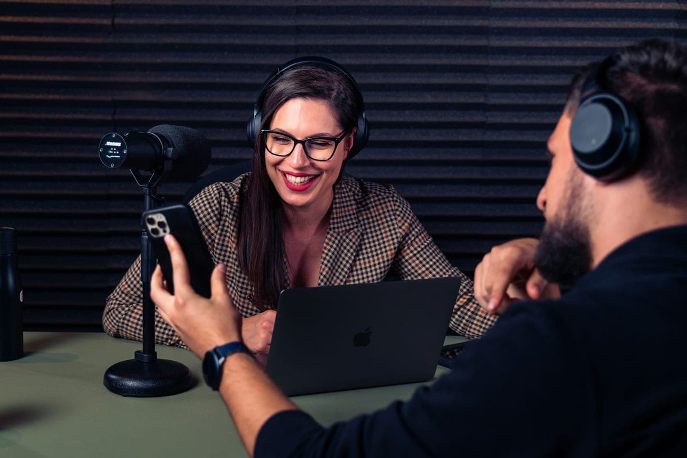 A creator coach and trainee reviewing content together on a laptop and smartphone in a professional studio with a broadcast microphone.